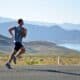 man running on side of road with lake and mountains in the background
