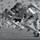 athletes running on track and field in grayscale